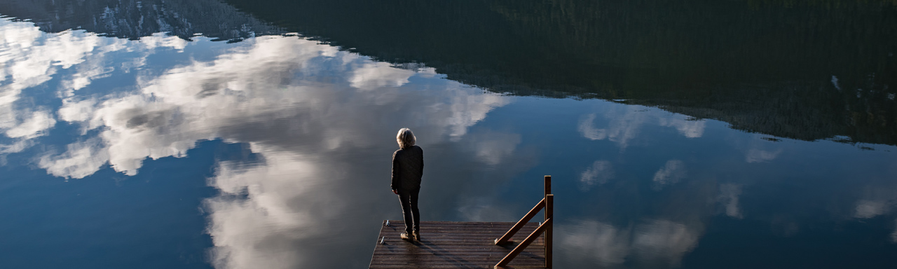 View from behind of person standing on dock looking across water